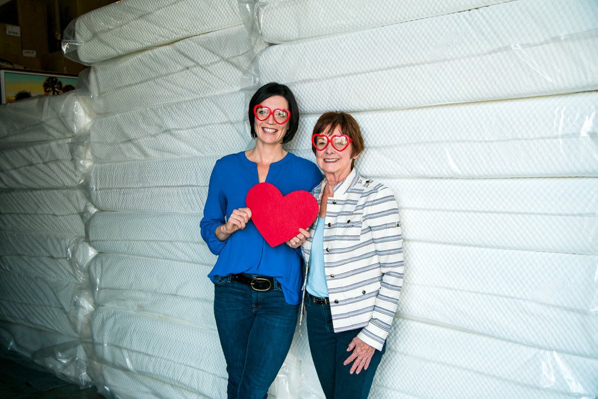 Robyn Phillips and her mother, Beth, pose with stacks of donated mattresses at the Furnishing Hope warehouse